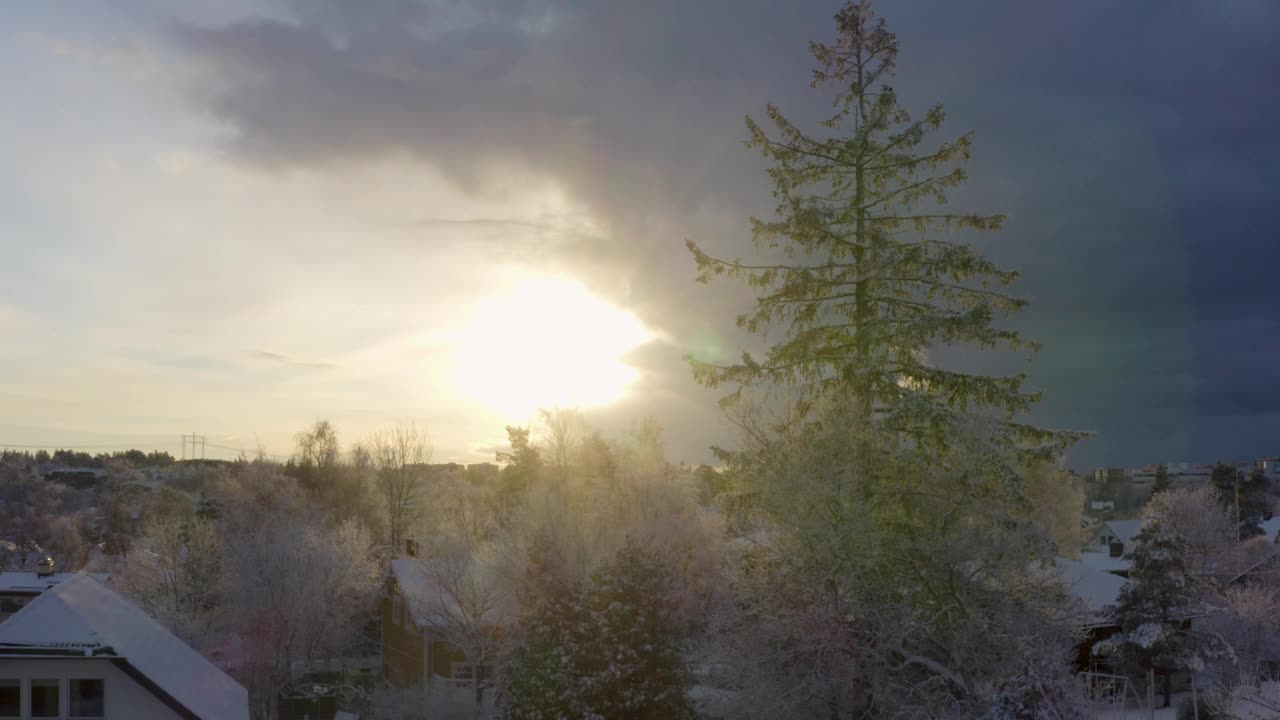 离开的无人机在白雪覆盖的别墅区上空盘旋，捕捉到前方的阳光。视频下载