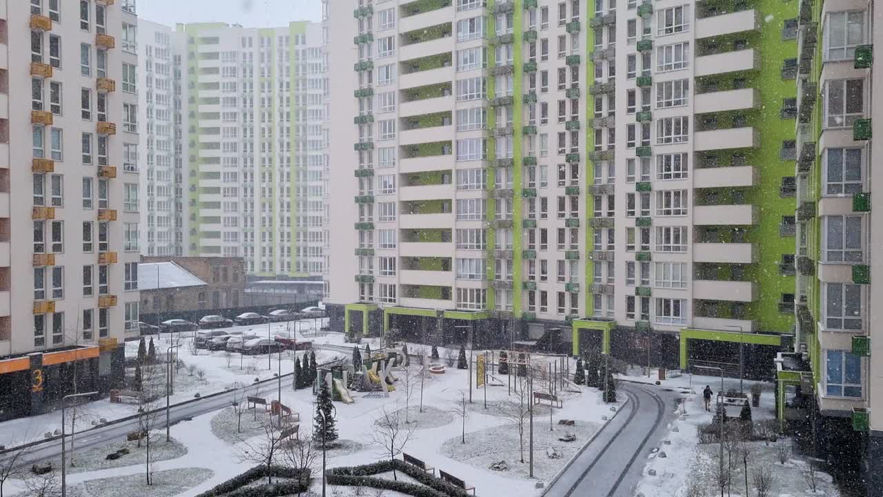 冬季景观，大雪在城市，窗口从一个新的现代公寓大楼外面，第一场雪在城镇视频下载