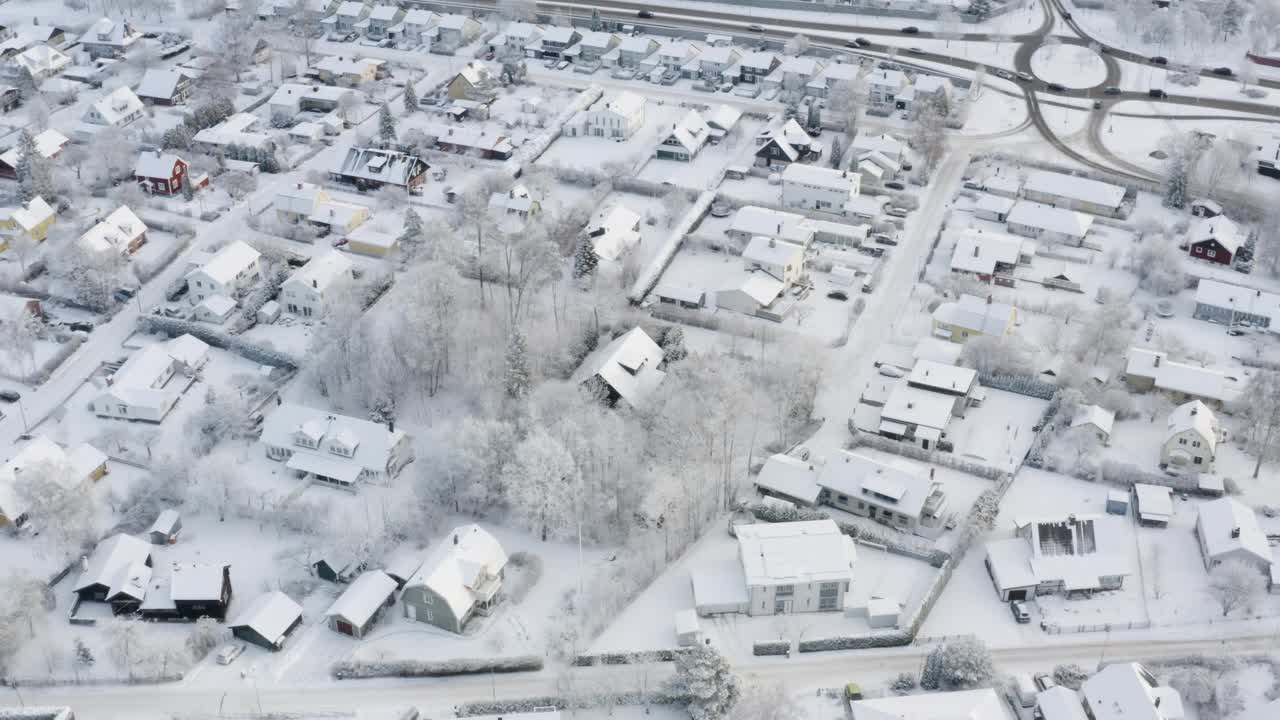 在一个宁静的冬季住宅区，旋转无人机拍摄了白雪覆盖的街道和移动的交通。视频下载