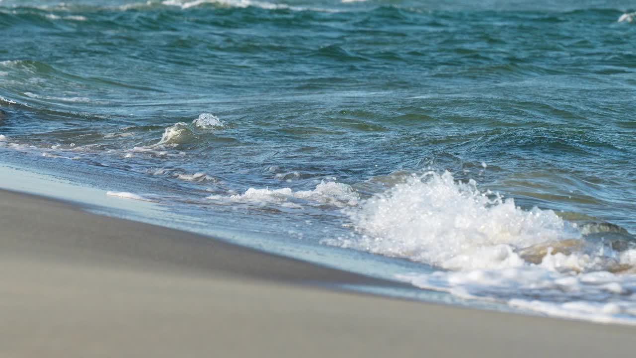 海浪轻轻地拍打着海岸，带着白色的泡沫，平静而安详。视频素材