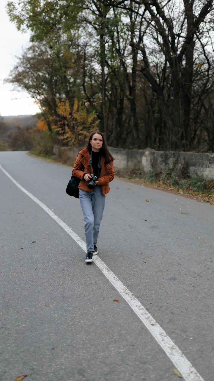 年轻的女性旅行者带着相机，拍摄鸟类，动物，风景。秋天，一名女游客独自旅行，背着背包在相机前拍照。垂直视频视频下载