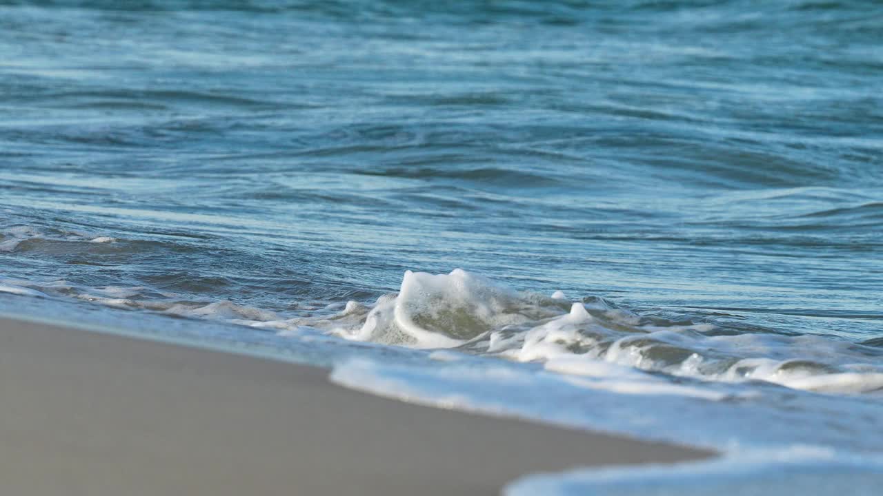 柔和的海浪拍打着阳光普照的沙滩。视频素材