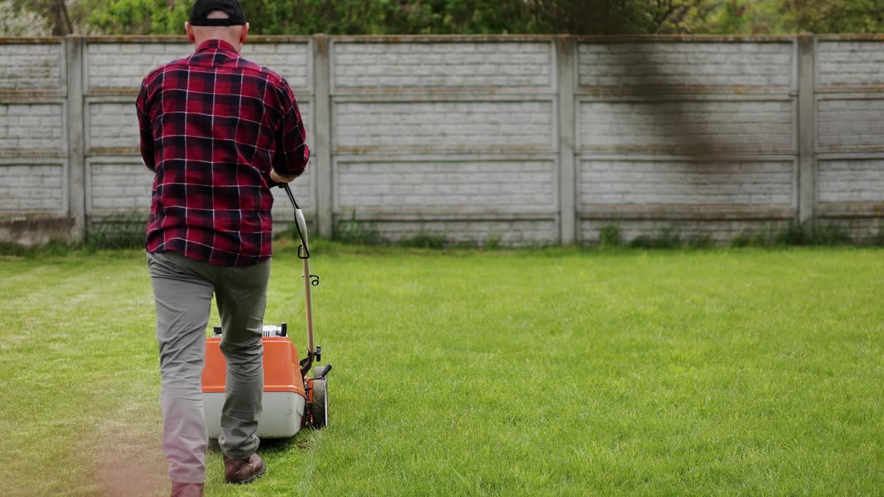 在他家后院，穿着便服的男子正在用割草机割草。春日阴天，丈夫照料花园。现代汽油园林设备。绿化工作视频素材