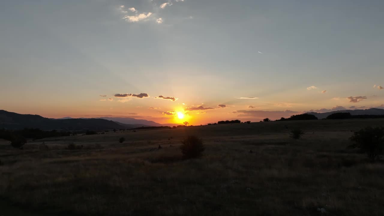 夕阳落在山的地平线上一棵孤零零的树后面。用低空飞行的无人机拍摄大自然的电影镜头。暖色调的天空和明亮的橙色太阳是放松的时刻。视频素材