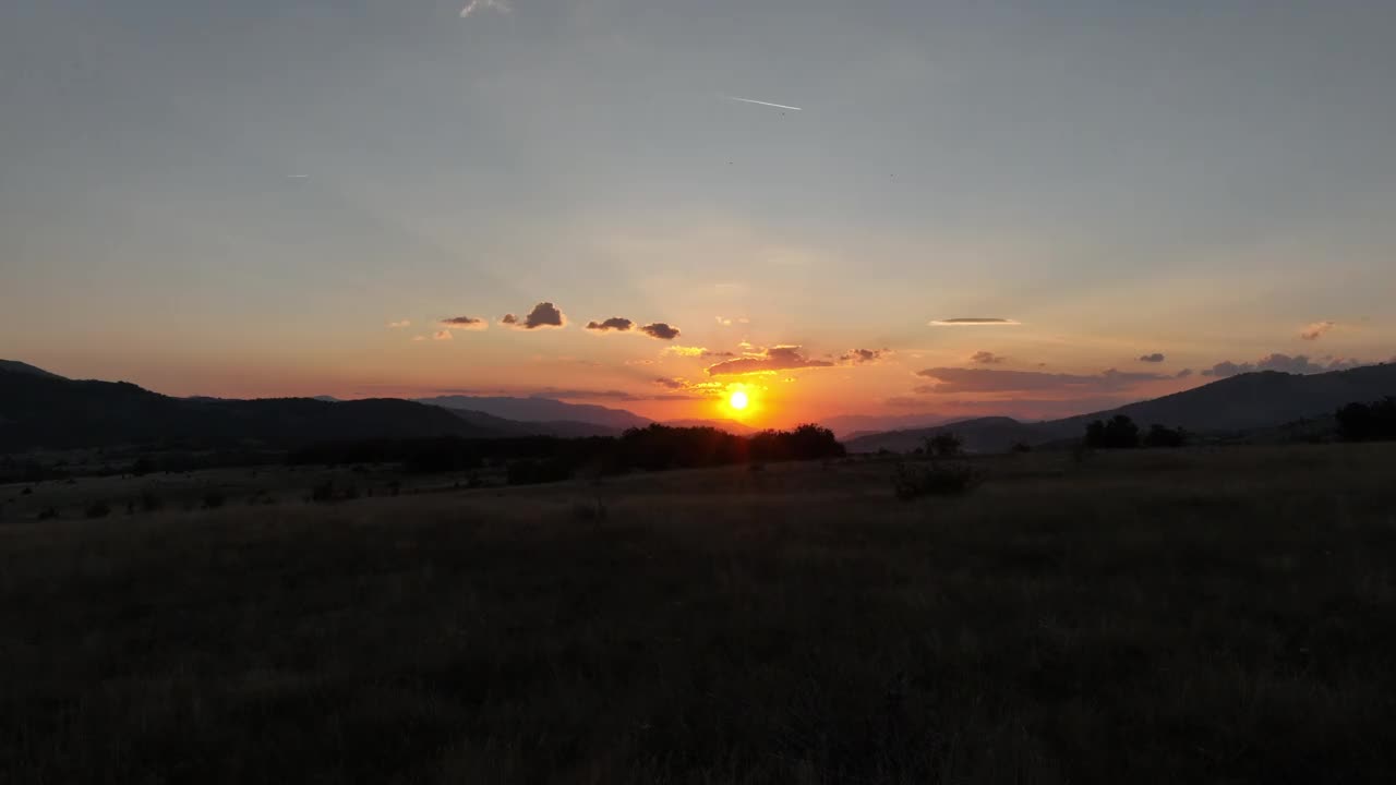 高原上一棵孤零零的树后的夕阳。用低空飞行的无人机拍摄大自然的电影镜头。暖色调的天空和明亮的橙色太阳是放松的时刻。视频素材