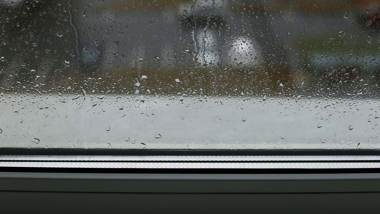 从屋内望向街道，雨滴落在窗台和双层玻璃上。秋天天气寒冷。文本的复制空间，凹陷视频素材