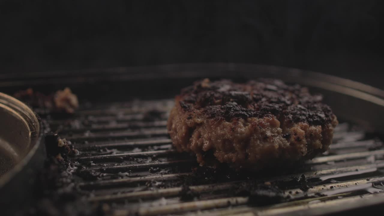 生牛肉或鸡肉汉堡，烤架上冒着浓烟，准备一个美味的汉堡三明治，然后带走，黑色背景和简单的光线设置在Raw 4K上拍摄视频素材