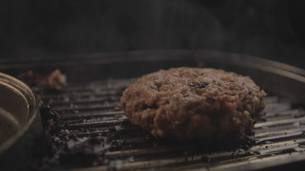 生牛肉或鸡肉汉堡在烤架上准备一个美味的汉堡三明治和翻转，黑色背景和简单的光设置在Raw 4K拍摄视频素材