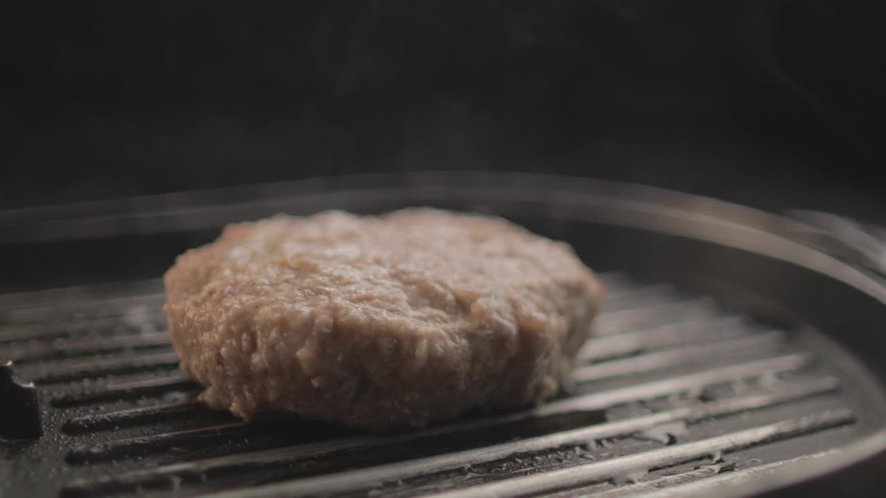 牛肉或鸡肉汉堡烤架上的肉正在准备美味的汉堡三明治，黑色背景和简单的光线设置在RAW 4K上拍摄视频素材