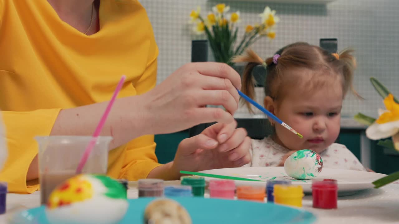 一位幼儿园老师教一个小女孩为复活节装饰彩蛋。孩子的特写。儿童教育的理念视频素材