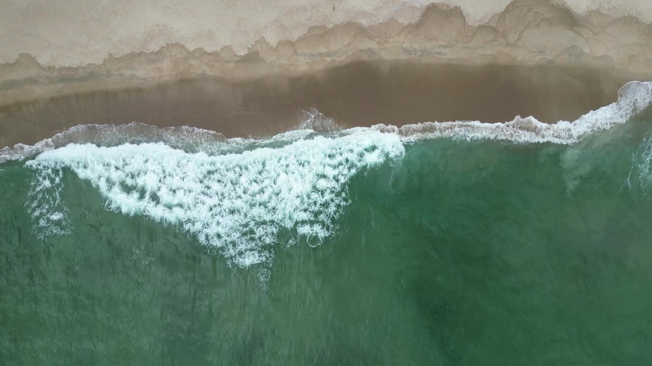 鸟瞰海岸的一个海滩，有波浪，岩石，多云的天空视频下载