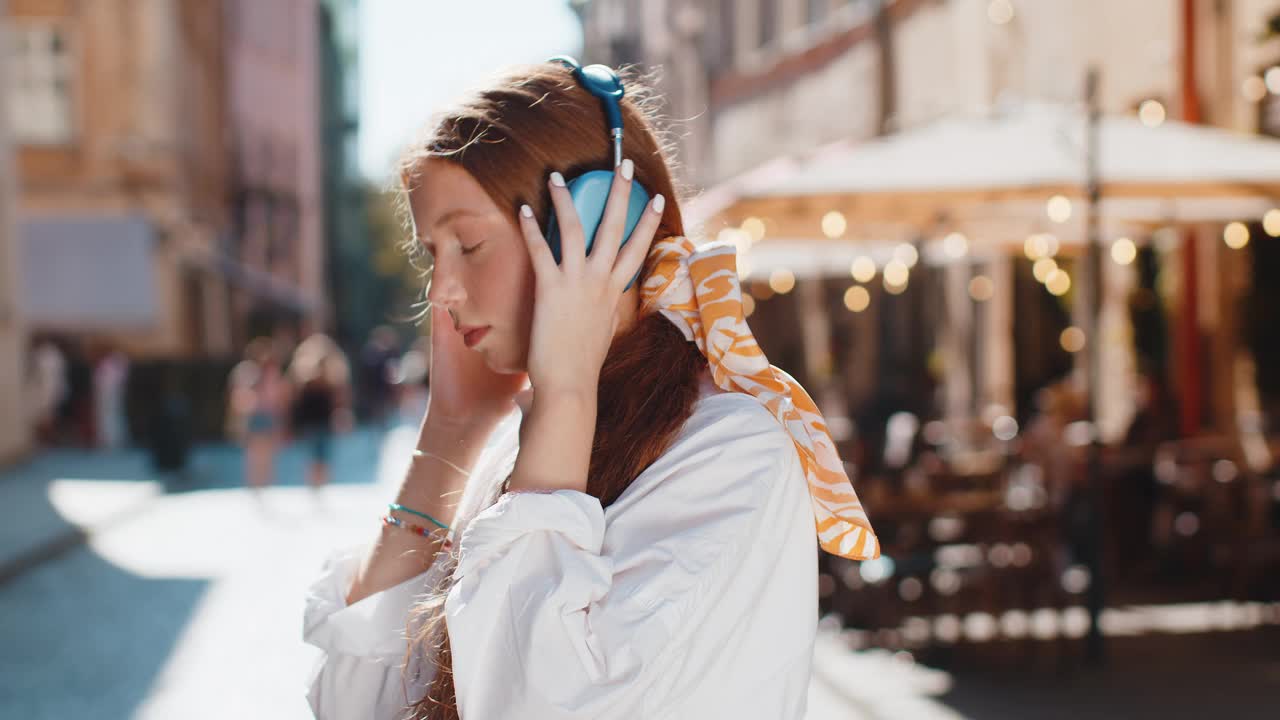 快乐的成年儿童女孩在无线耳机选择，听音乐跳舞户外城市街道视频素材