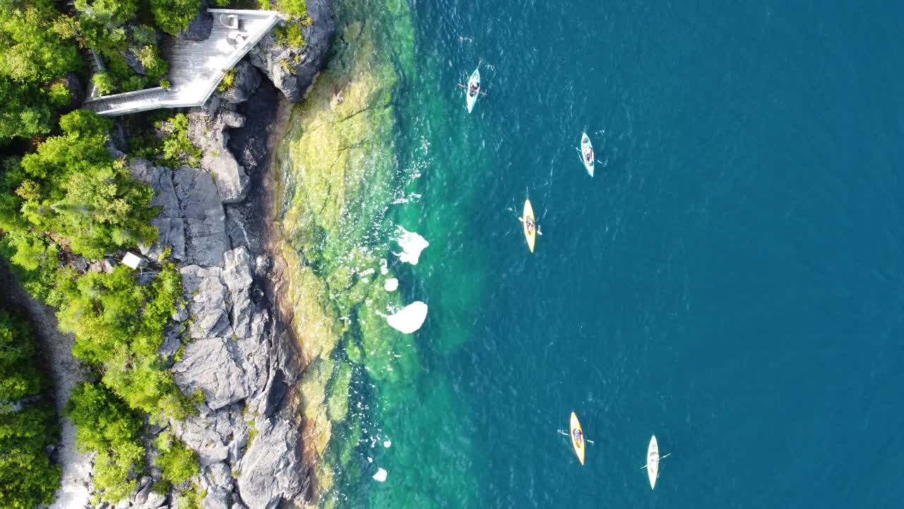 在清澈的海水中沿着岩石海岸划独木舟。空中无人机。视频素材