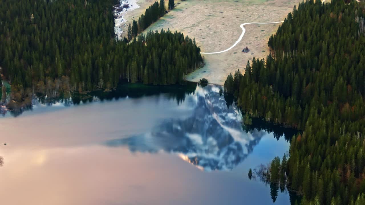 空中无人机拍摄的雪山映照在茂密森林环绕的湖上视频素材