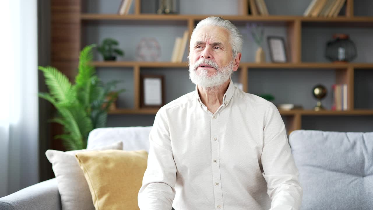 耳痛。生病的老人坐在家里的沙发上遭受耳朵疼痛。视频素材