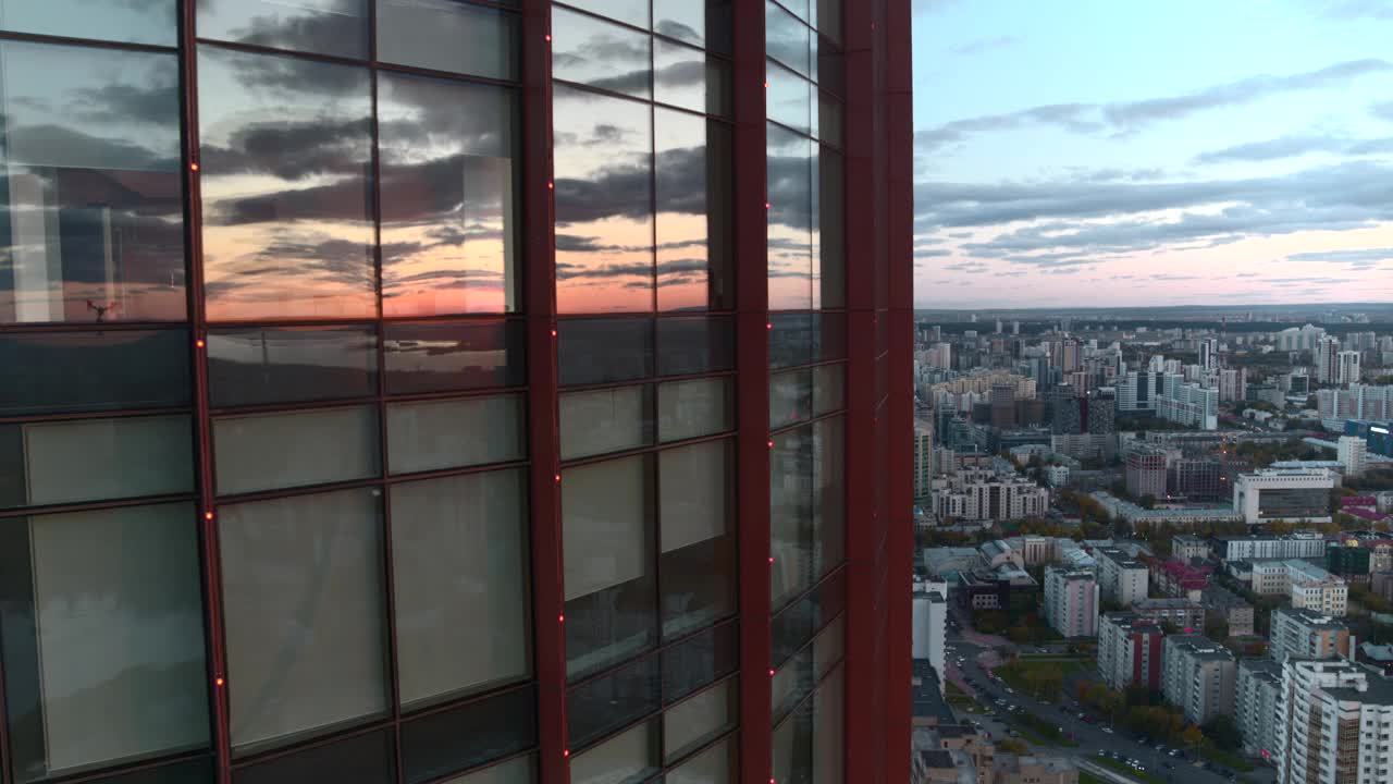 现代玻璃办公摩天大楼的鸟瞰图，窗外反射出城市景观。资料片。在一个夏日的夜晚飞过这座现代化的城市视频素材