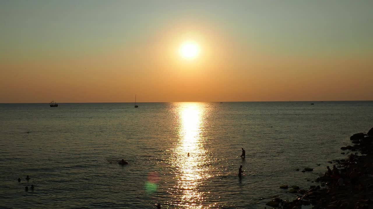 天堂海滩日出。夕阳掠过黑海，海浪冲刷着沙滩。水面上阳光明媚的小路。游客们在黎明时游泳和晒日光浴。日出，日落，黎明。旭日盘。视频素材