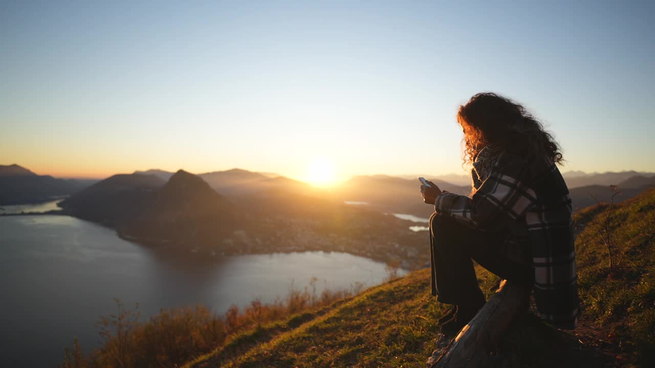 一个女人独自坐在视点，看她的智能手机视频下载