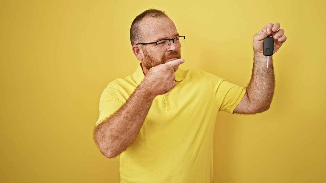 白人男子微笑着自信地指着新车的钥匙，在孤立的黄色背景上庆祝视频素材