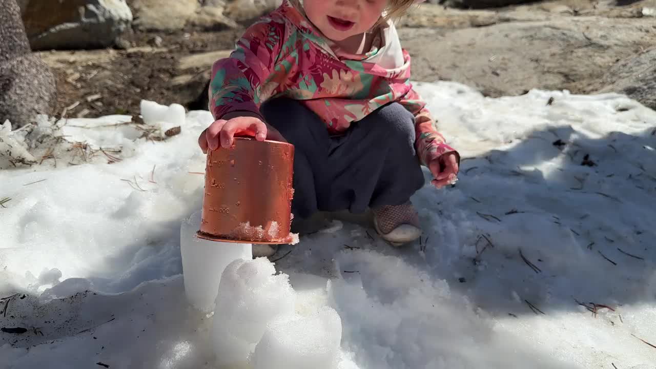 初学走路的孩子在春天的雪地里拿着杯子玩耍视频下载