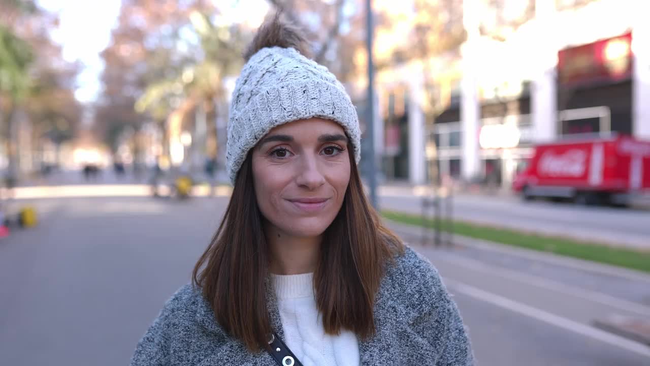 冬日里，站在城市街道上的一位开朗的年轻女子对着镜头微笑视频素材