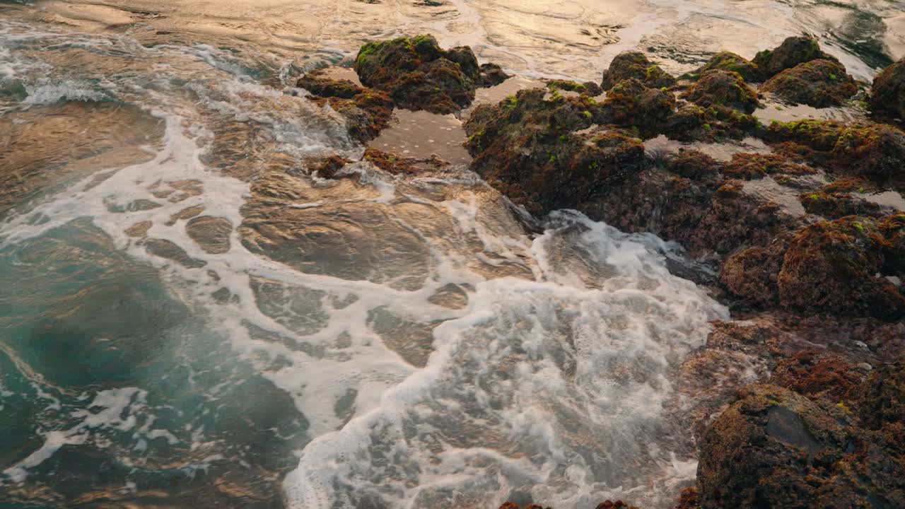 汹涌的海浪冲击着火山岩海岸线的特写镜头。蓝绿色的海水拍打着海岸。温暖的金色小时色。视频素材