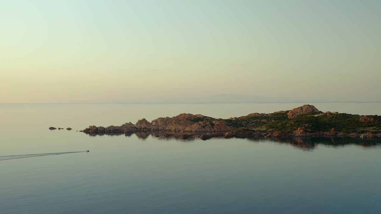 日落时分，意大利撒丁岛Isola Rossa海滩地区Punta Canneddi红色岩石景观中的一艘摩托艇的无人机鸟瞰图视频素材