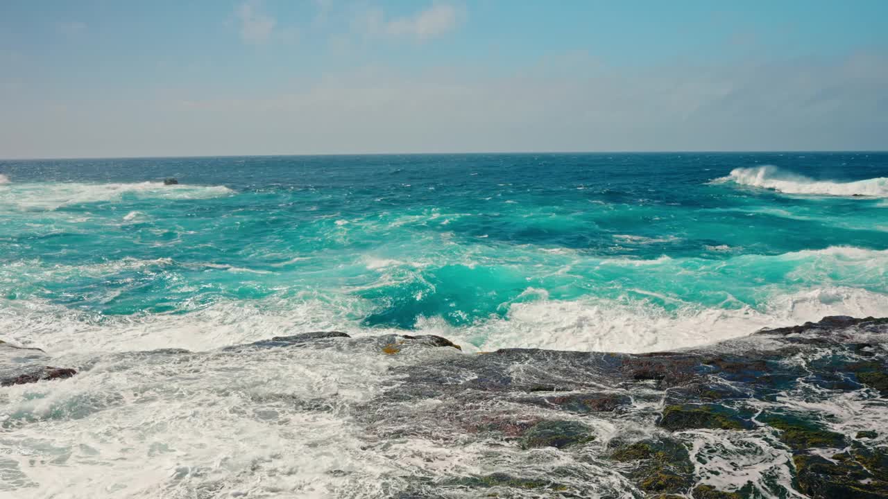 波涛汹涌的海浪冲击着布满火山岩的海岸线的慢镜头。蓝绿色的海水拍打着海岸。晴天，晴空万里。视频素材