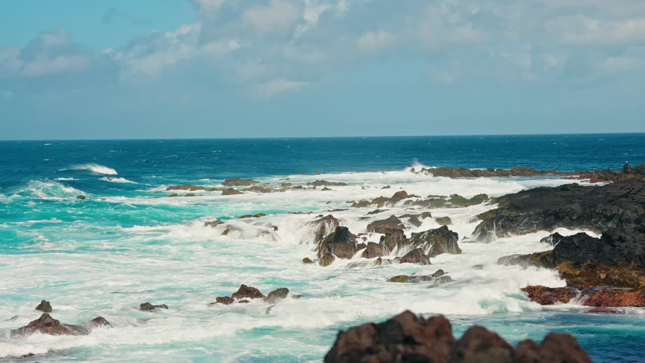 慢动作静态特写拍摄汹涌的海浪冲击着火山岩海岸线。蓝绿色的海水拍打着海岸。晴天，晴空万里。视频素材