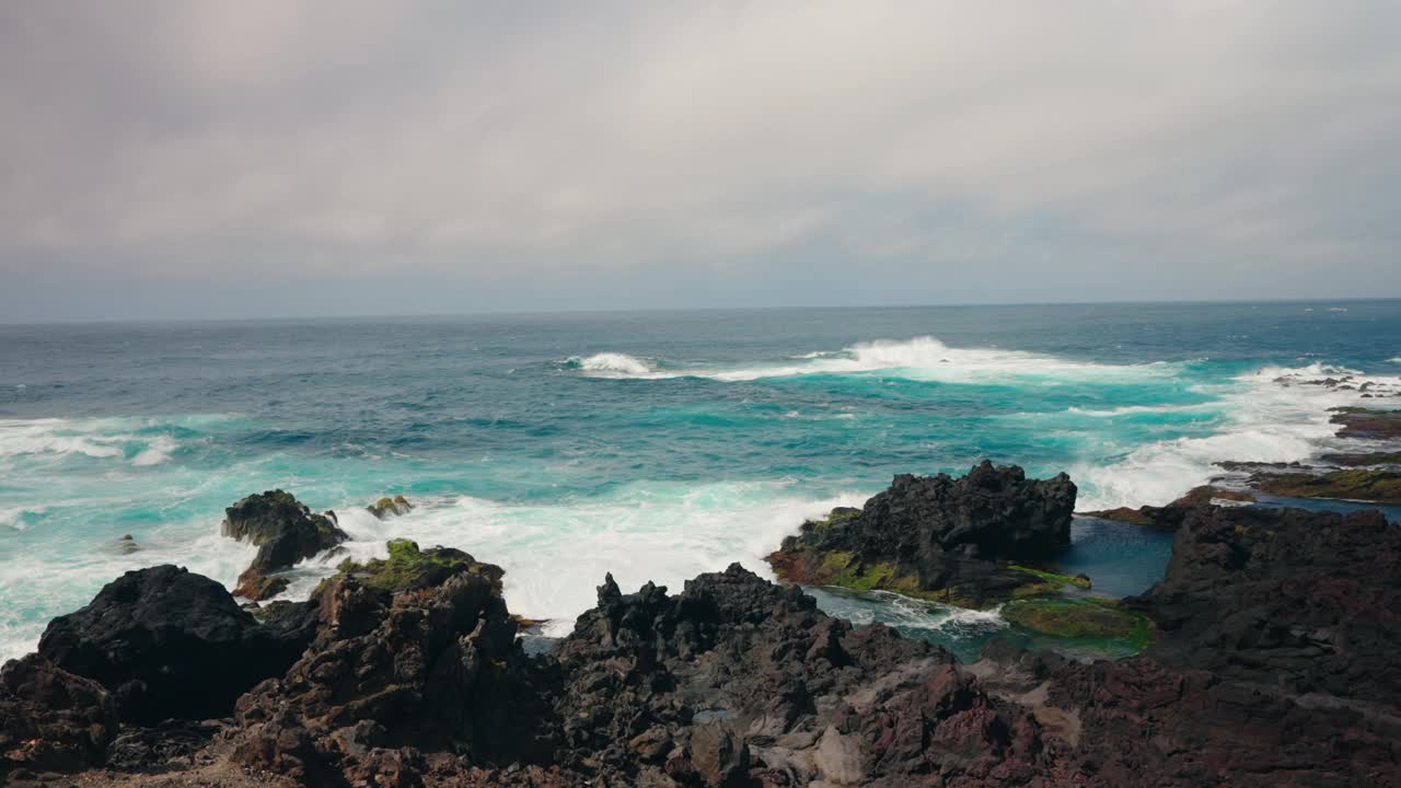 波涛汹涌的海浪冲击着布满火山岩的海岸线的慢镜头。蓝绿色的海水拍打着海岸。晴天，晴空万里。视频素材