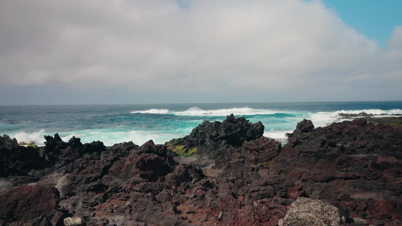 波涛汹涌的海浪冲击着布满火山岩的海岸线的慢镜头。蓝绿色的海水拍打着海岸。晴天，晴空万里。视频素材