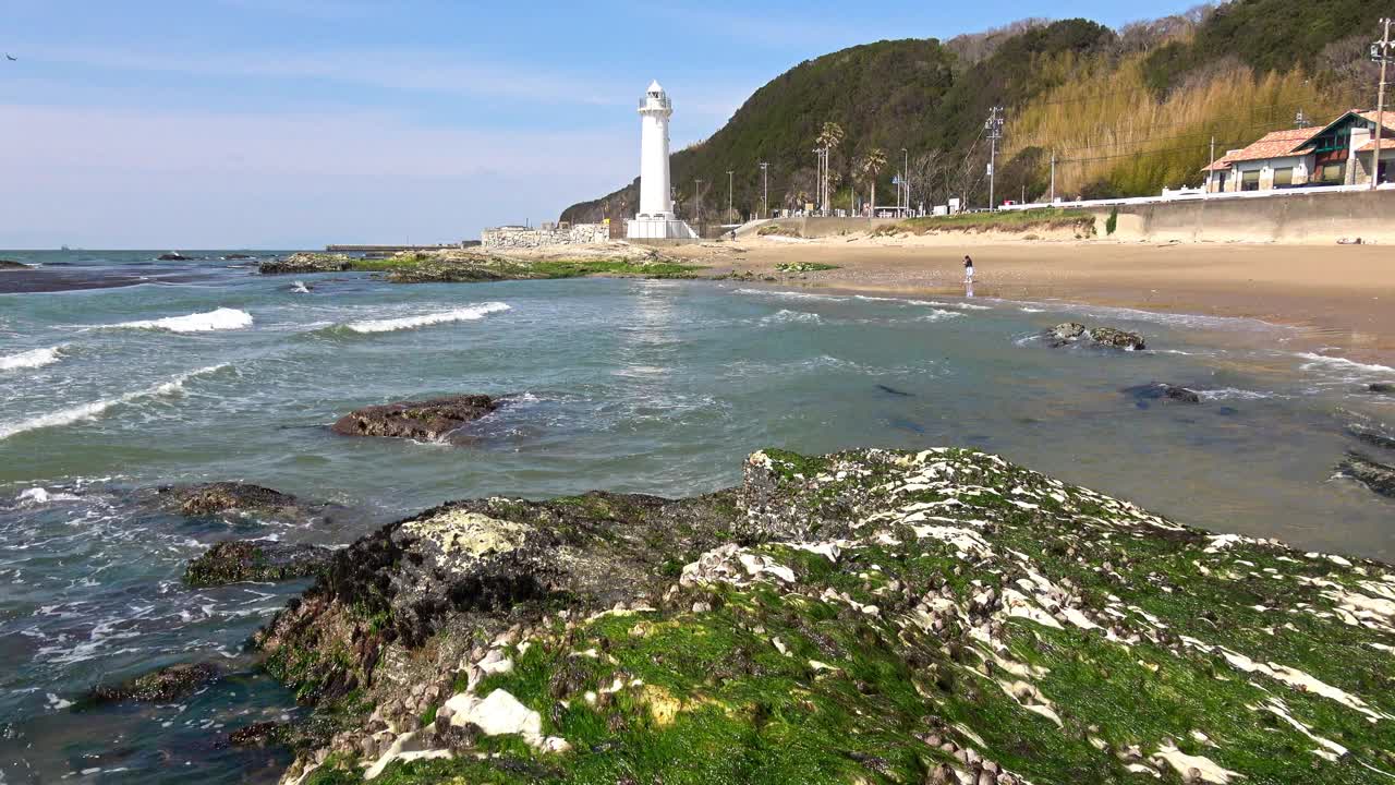 海浪拍打着沙滩，背景是灯塔视频素材