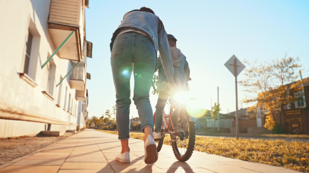 小男孩第一次骑自行车。年轻的妈妈帮助儿子骑自行车。妈妈在城市公园教她的小儿子骑自行车。幸福的家庭时光。时间在一起的母亲和儿子。视频素材