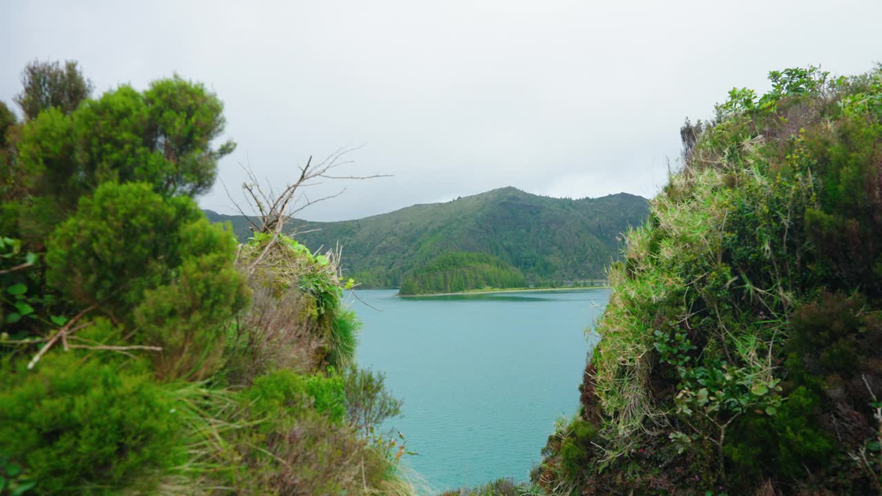 穿过郁郁葱葱的植被，亚速尔群岛风景如画的火山湖一览无遗。Lagoa do Fogo，圣米格尔岛。背景中绿色山脉的景色。视频素材