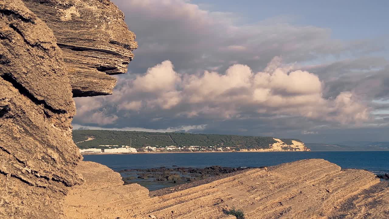 海滩上岩石形成的壮观延时视频，海浪正在撞击海岸线。低角度阳光。水面对面的小住宅区可见。视频素材