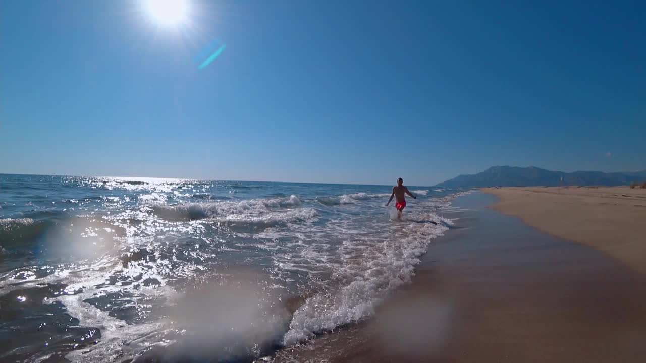 穿着泳裤的男子在热天的海上在水面上奔跑，挥手视频素材