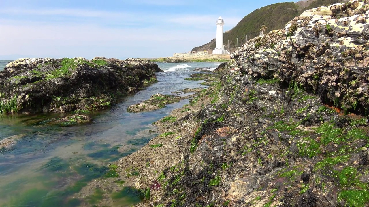 海浪拍打着岩石海岸，背景是灯塔视频素材