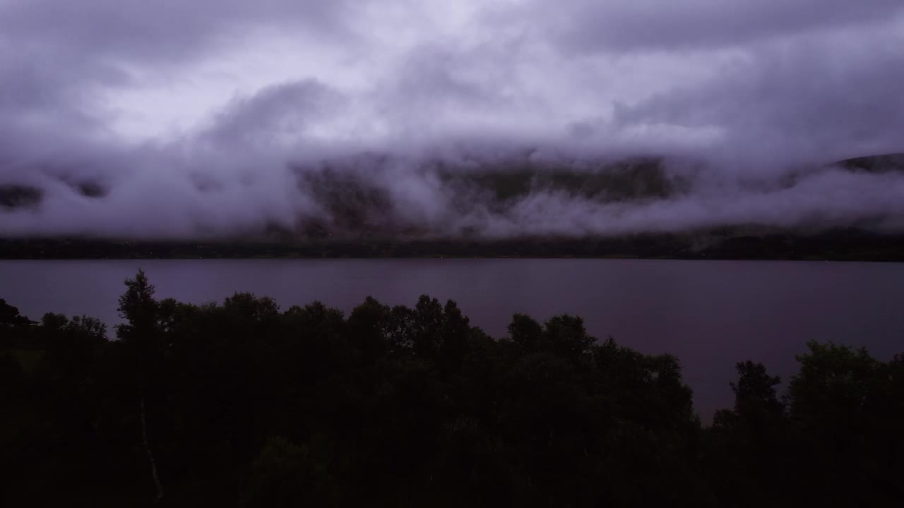 在夜晚飞过树梢和山湖，在斯堪的纳维亚半岛的水面上低空的云层视频素材