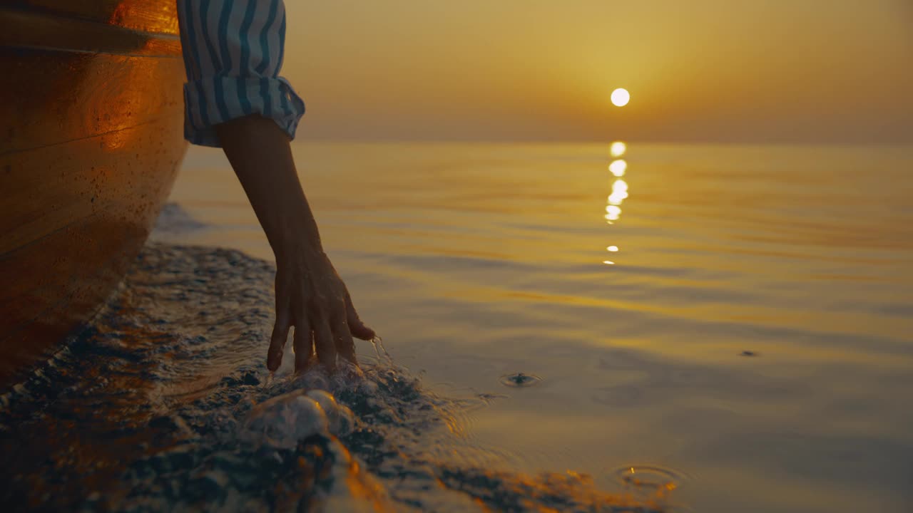 日落时分，一名无法辨认的女子在船上航行，用手触摸着海面视频素材