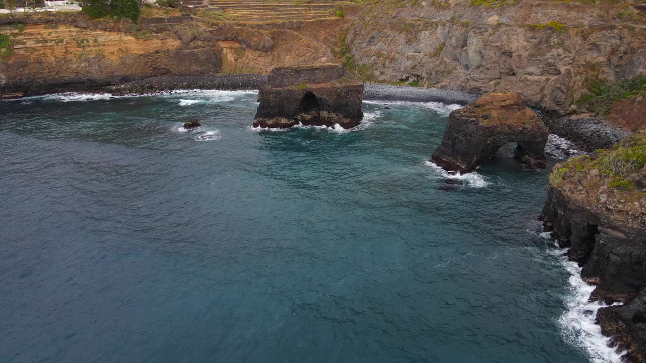 在一个阳光明媚的日子里，在特内里费岛洛斯罗克海滩上的火山岩层的轨道上拍摄的梦幻般的航拍照片。视频素材