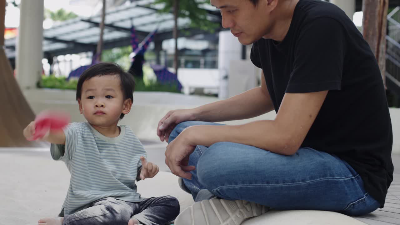 可爱的亚洲小男孩和爸爸在公园操场的沙箱里玩沙。幼儿户外活动学习实验概念。视频素材