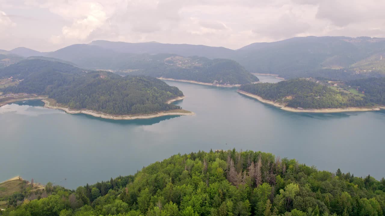 航拍画面，多云的天气里，绿树成荫的山丘环绕着Zaovine的蓝色湖泊视频素材