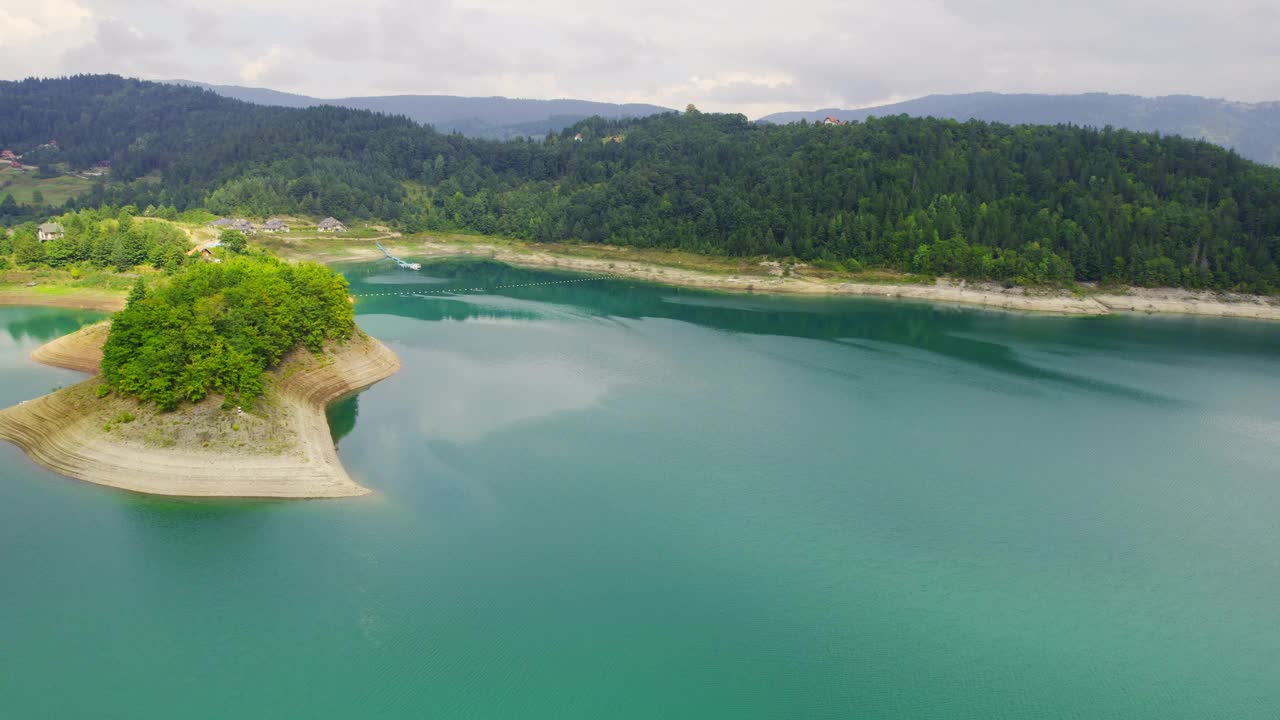 无人驾驶飞机在清澈的蓝色湖岸上空飞行，周围环绕着小山和树林视频素材