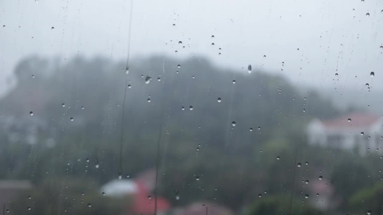 雨滴落在窗户表面的玻璃上，以丘陵自然景观为背景。外面的大雨和室内公寓的景色。视频素材