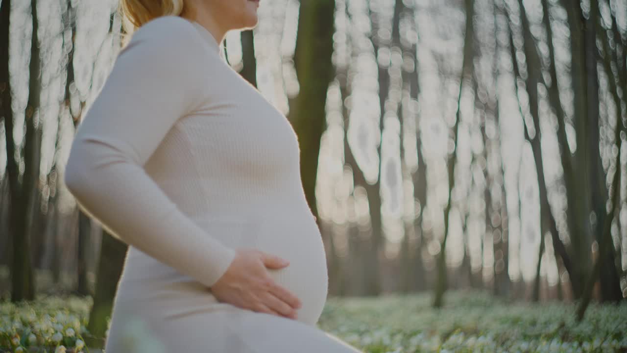 春天的树林里，穿着白色连衣裙的孕妇抱着肚子视频素材