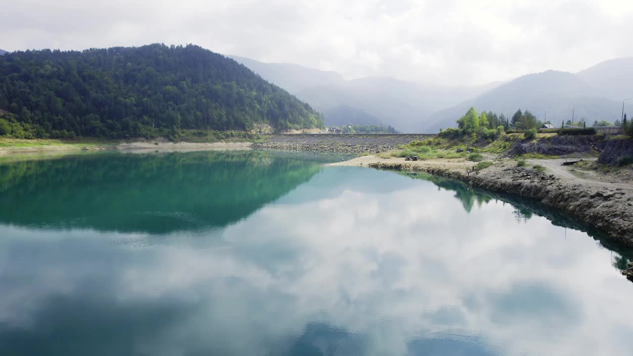 在塞尔维亚的Zaovine，无人机在蓝色的湖面上飞向浓雾中的山脉视频素材