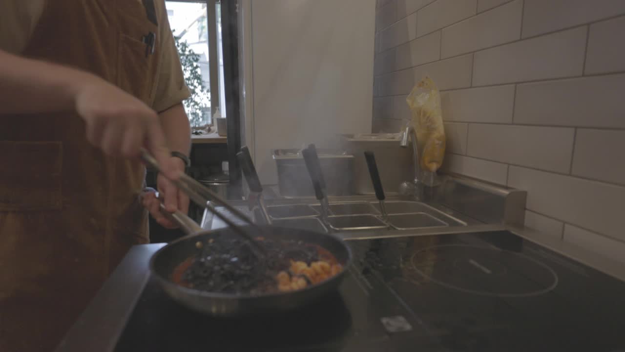 黑色意大利面食烹饪过程。煮熟的黑意大利面与酱汁和配料混合在热锅里。意大利菜，传统食谱。慢动作，ProRes 422, 10比特，未分级的C-LOG视频视频素材