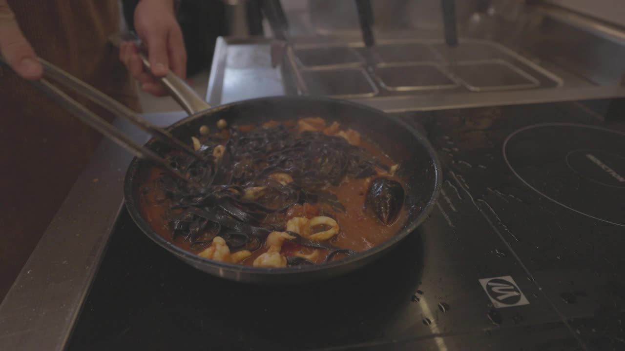 黑色意大利面食烹饪过程。煮熟的黑意大利面与酱汁和配料混合在热锅里。意大利菜，传统食谱。慢动作，ProRes 422, 10比特，未分级的C-LOG视频视频素材