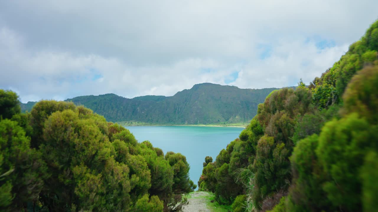 穿过郁郁葱葱的植被，亚速尔群岛风景如画的火山湖一览无遗。Lagoa do Fogo，圣米格尔岛。背景中绿色山脉的景色。视频素材