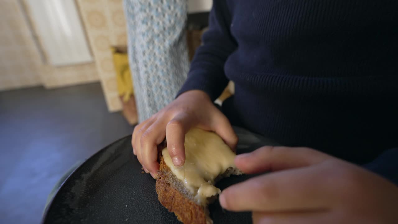 小男孩在厨房地板上吃面包和奶酪——享受碳水化合物食物视频素材